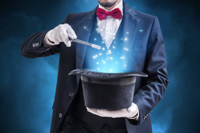 Magician or illusionist is showing magic trick. Blue stage light in background.